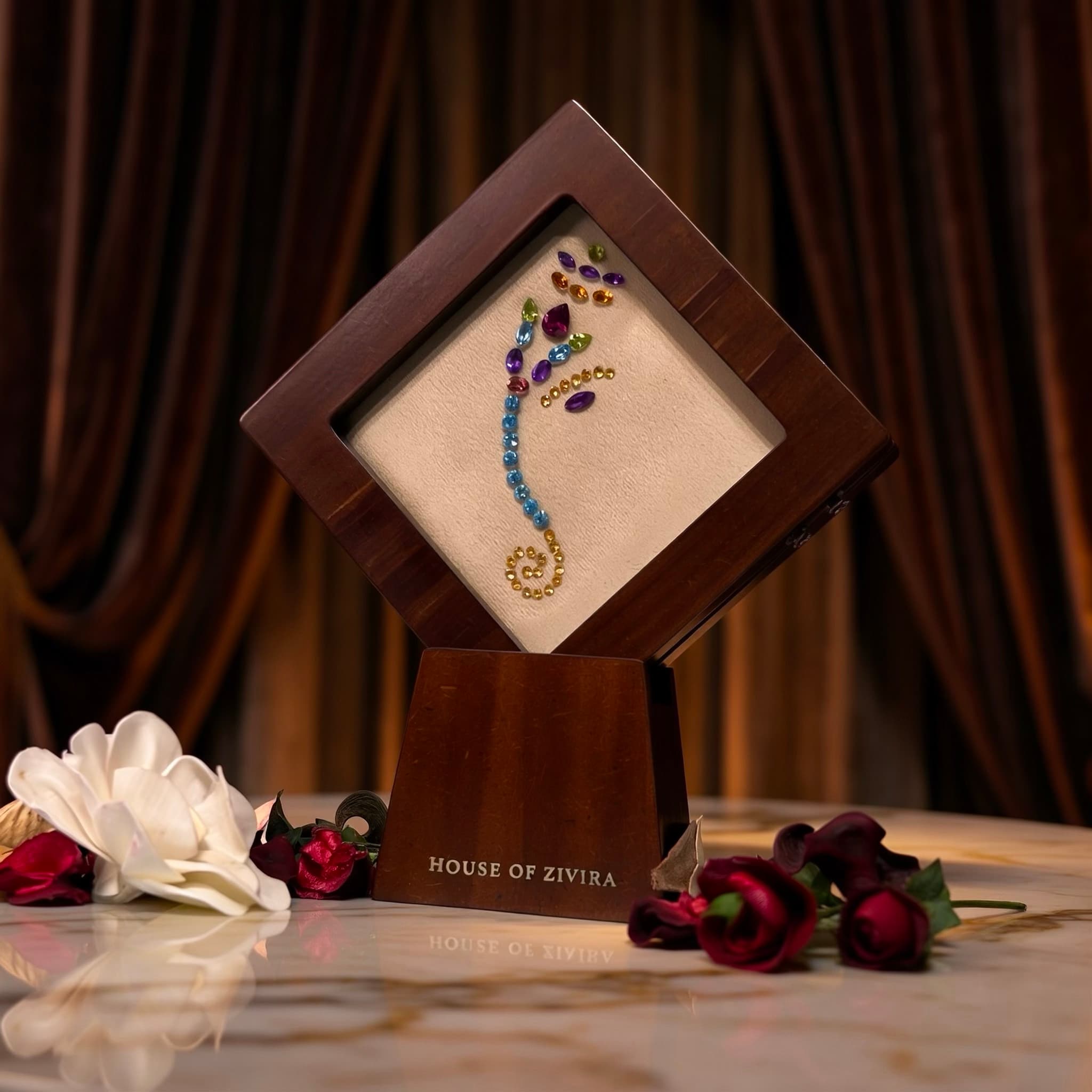 Ganesh side profile in natural gemstones on its own stand, beside marigolds and a lit brass diya