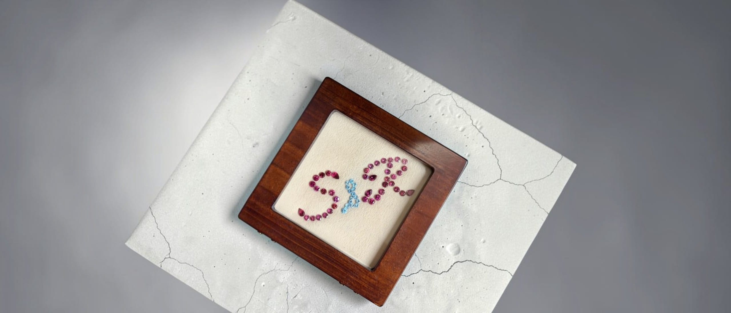 The joined initials S and R set in rhodolite garnet and blue topaz, framed in walnut, photographed from above